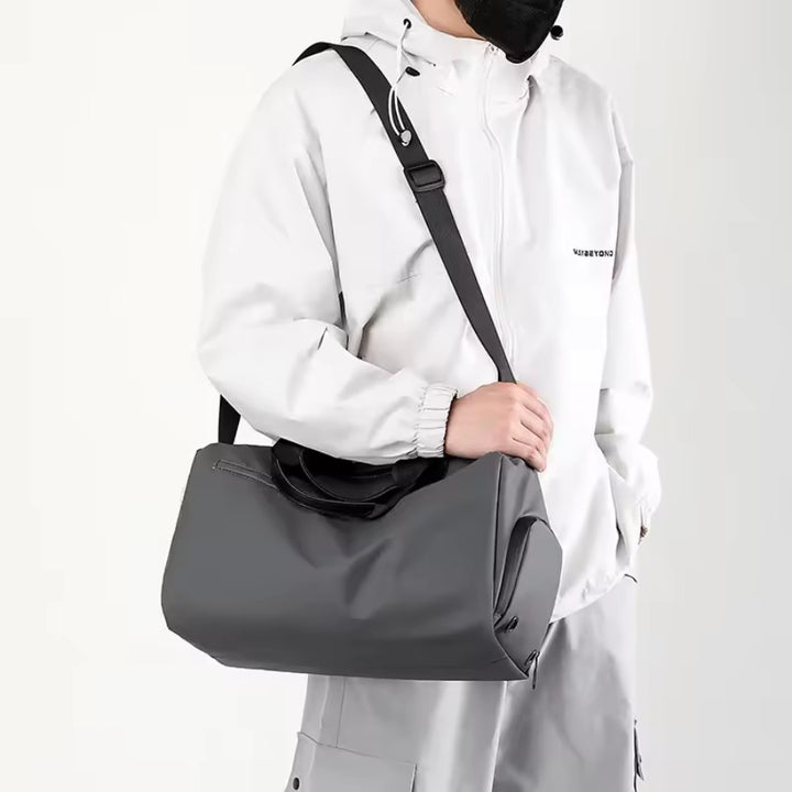 Petit sac de voyage homme gris porté en bandoulière, format cabine, design minimal pour week-end et salle de sport.