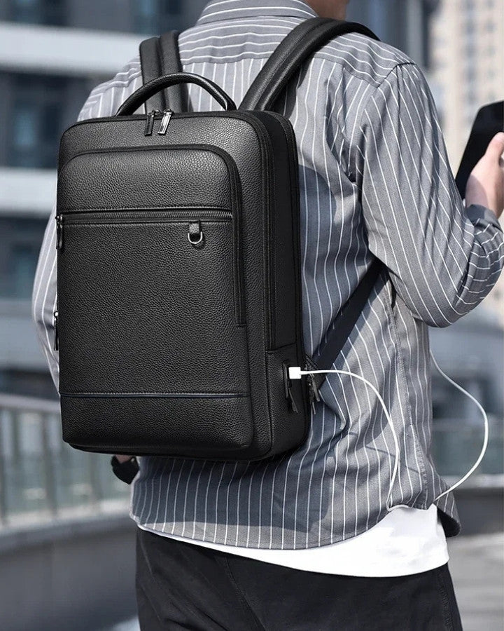 Sac à Dos Simili Cuir Homme, porté sur le dos d'un homme tenant son téléphone portable en main, en charge avec le port USB intégré au sac